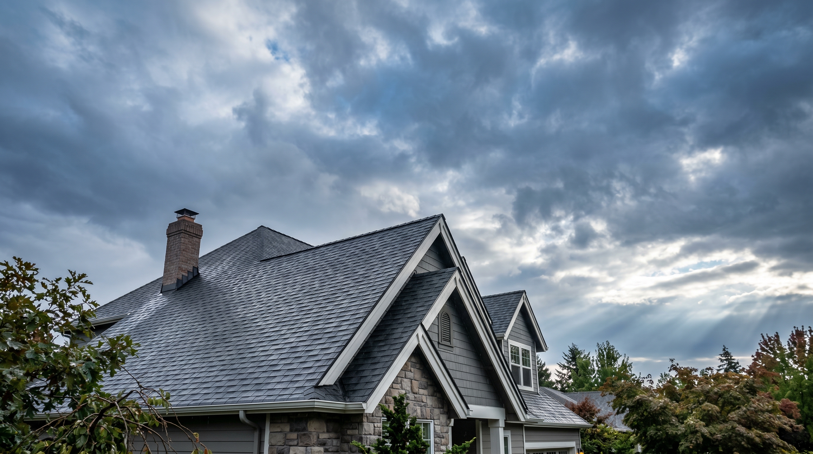 A gabled suburban roof with crisp architectural shingles under a sky clearing after a storm.